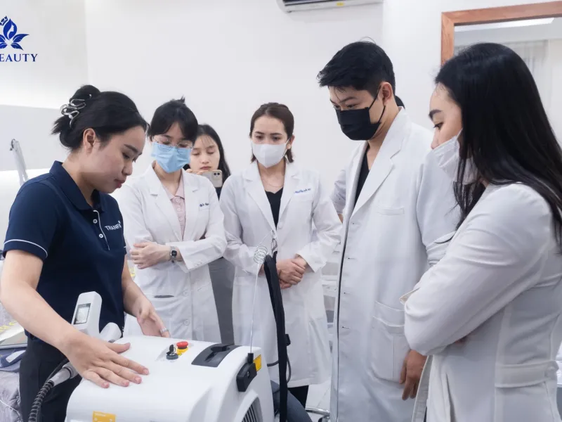 Nhân viên và người mặc áo blouse trắng quan sát thao tác trên thiết bị màu trắng tại phòng khám